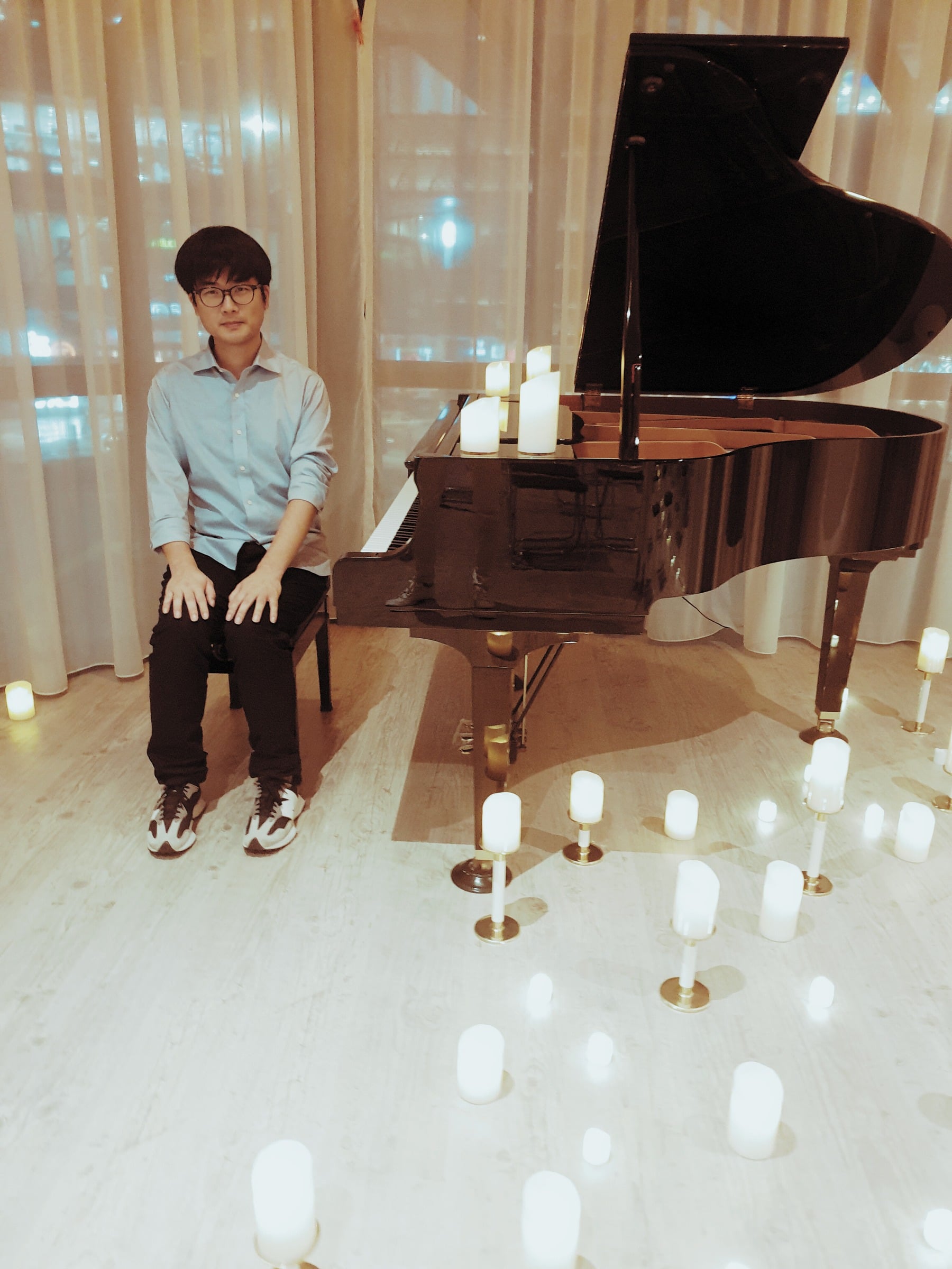 Jaeyong Kang seated beside a grand piano surrounded by candlelight