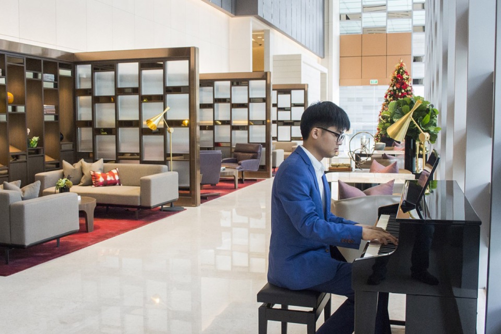 Jaeyong Kang in a blue suit playing an upright piano in a hotel lobby
