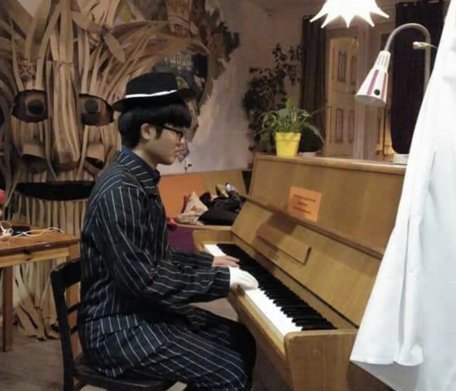 Jaeyong Kang in a pinstripe outfit and hat playing an upright piano in Prague