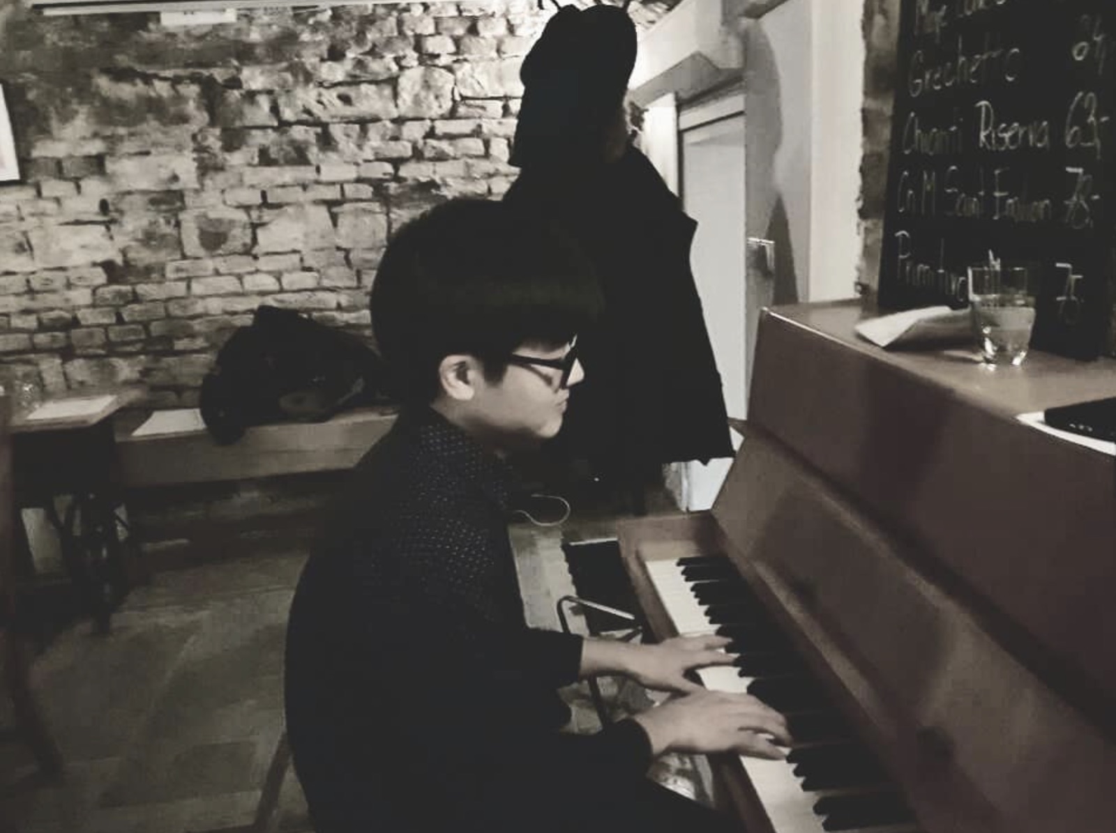 Black-and-white photo of Jaeyong Kang playing an upright piano in a wine bar